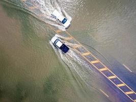 caminos inundados, gente con autos corriendo. la fotografía aérea de drones muestra calles inundadas y autos de personas que pasan, salpicando agua. foto