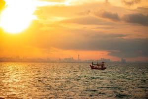 A small fisherman boat floats alone in the sea in the morning against the backdrop of a big city. photo