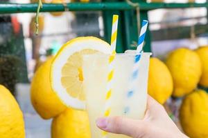 Caucasian hand with healthy fresh lemonade during summer - lemons background photo