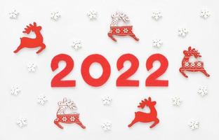 tarjeta de felicitación de año nuevo 2022 con renos rojos de santa y copos de nieve blancos. decoraciones de madera y números de fieltro año 2022. revisión del año. foto