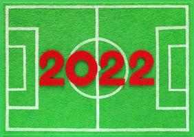 Red felt year numbers 2022 placed on mini football field made of green felt, top view. Concept about schedule of soccer championship matches. Background with copy space. photo