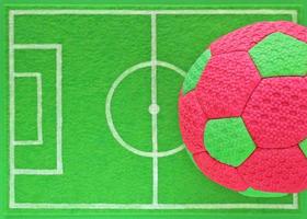 Colorful pink and green kid's soccer ball on mini football field made of green felt, top view. Banner for children's team sports section or camp, indoor at school, outdoor at stadium. Copy space.