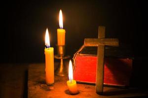 velas encendidas con la sagrada biblia y la cruz o el crucifijo sobre un fondo de madera antiguo en la iglesia. luz de las velas y libro abierto sobre una mesa de madera vintage estudio y lectura del cristianismo en el hogar. concepto de la religión de cristo foto