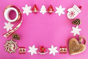 vista superior en el marco de decoraciones navideñas de madera roja y blanca y conos de pino en el fondo rosa con espacio para copiar. foto