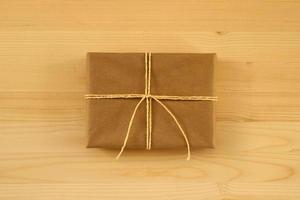 Gift box wrapped of craft paper and yellow ribbon on the wooden background, top view. photo