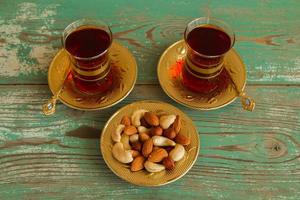 Mixed nuts on a yellow metal saucer and two glass cups of Turkish tea on a turquoise wooden background. photo