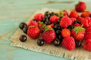 fresas, frambuesas y grosellas negras en las servilletas de tela de saco sobre el fondo de madera azul-blanco. foto