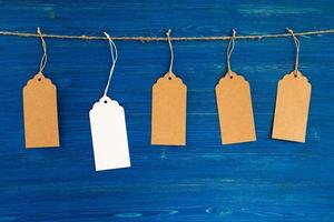 Five brown and white blank paper price tags or labels set hanging on a rope on the blue wooden background. photo