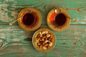 Mixed nuts on a yellow metal saucer and two glass cups of Turkish tea on a turquoise wooden background, top view. photo