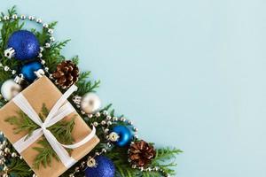 Christmas flat lay composition of fir branches with gift box and decorations at the left corner with copy space on the blue background. photo