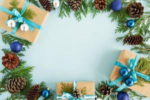 Top view on frame from Christmas decorations, gift boxes, fir branches and pine cones on the blue background with copy space. photo