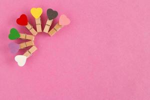 Wooden pins with colorful hearts on the pink background, top view. Decorations for Valentine Day. photo