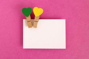 White sheet with green and yellow pins on the pink background for Valentine Day. Copy space. photo