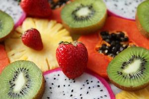 Las frutas y bayas mixtas maduras y frescas se cierran para el fondo. fruta del dragón, piña, papaya, kiwi, fresa. foto