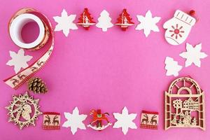 vista superior en el marco de decoraciones navideñas de madera roja y blanca y cono de pino en el fondo rosa con espacio para copiar. foto