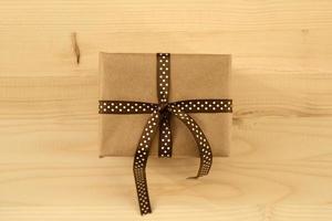 Gift box wrapped of craft paper and brown ribbon on the wooden background, top view. photo