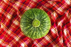 Green pumpkin on a red checkered towel, top view. Autumn still life. photo