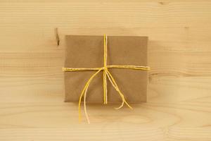 Gift box wrapped of craft paper and white and yellow ribbon on the wooden background, top view. photo