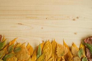 borde de hojas secas de otoño de colores sobre el fondo de madera, vista superior. foto