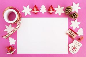 vista superior de las decoraciones navideñas, conos de pino y hoja blanca de papel sobre el fondo rosa con espacio para copiar. foto