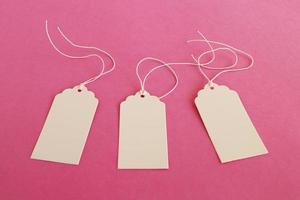 Three white blank paper price tags or labels set on the pink background. photo