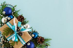 Christmas flat lay composition of fir branches with gift box and decorations at the left bottom corner with copy space on the blue background. photo