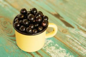 An orange metal cup with blackcurrant on the blue and white wooden background. photo