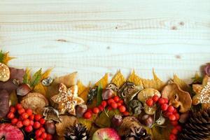Border from colorful autumn leaves, mushrooms, rose hips, rowanberry, apples, nuts, cones and cookies on the wooden background. Fall background. photo