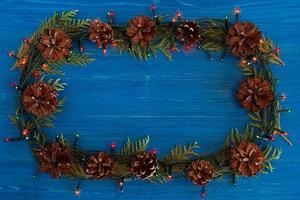 Top view on frame from Christmas lights, fir branches and pine cones on the blue wooden background with copy space. photo