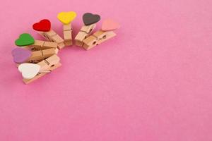 Wooden pins with colorful hearts on the pink background, top view. Decorations for Valentine Day. photo
