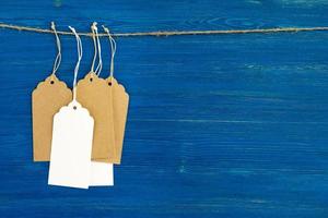 Etiquetas o etiquetas de precio de papel en blanco marrón y blanco colgadas en una cuerda sobre el fondo de madera azul. foto