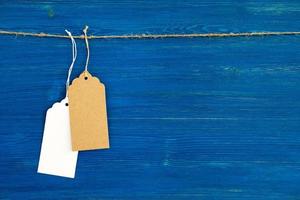 Two brown and white blank paper price tags or labels set hanging on a rope on the blue wooden background. photo
