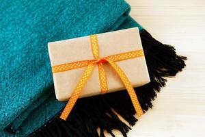 Gift box wrapped of craft paper and orange ribbon on a turquoise and black woolen plaid on the wooden background, top view. photo