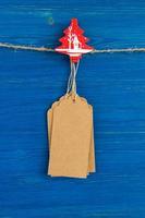 juego de etiquetas o etiquetas de precio de papel en blanco marrón y decoración de madera de navidad colgando de una cuerda en el fondo de madera azul. foto