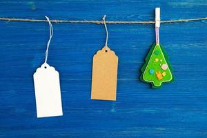 Brown and white blank paper price tags or labels set and Christmas felt decorations hanging on a rope on the blue wooden background. photo