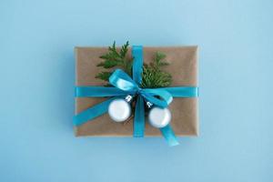 Gift box wrapped of craft paper, blue ribbon and decorated fir branches and silver Christmas balls on the blue background, top view. Christmas present. photo