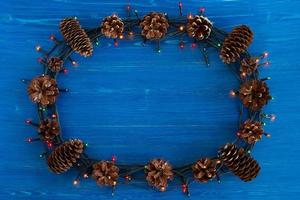 Top view on frame from Christmas lights and pine cones on the blue wooden background with copy space. photo