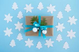 Gift box wrapped of craft paper, blue ribbon and decorated fir branches and silver Christmas balls on the blue background with paper fir tree and star, top view. Christmas present. photo