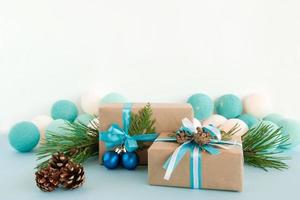 Two Christmas gift boxes wrapped of craft paper, blue and white ribbons, decorated of fir branches, pine cones and Christmas balls on the blue and white background with Christmas lights. photo