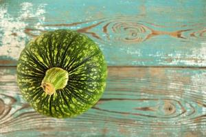 Small green pumpkin on a vintage turquoise wooden background, top view. Autumn still life. photo