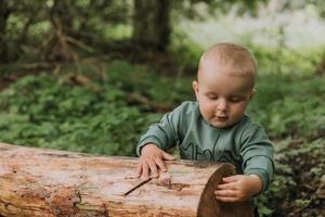 retrato de un lindo bebé aferrándose a un tronco en el fondo de un bosque verde. canasta de calabaza para dulces en primer plano. caminar y jugar al aire libre. concepto de Halloween. foto de alta calidad