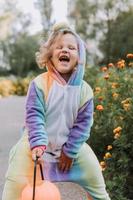 cute little girl in a rainbow unicorn costume for Halloween goes to collect sweets in a pumpkin basket in a residential area. child walks in the outdoor. trick or treat. lifestyle. kigurumi photo