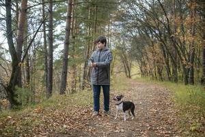 A happy and joyful boy walks with his buddy, a Boston terrier puppy, in a beautiful golden autumn forest. A child plays and has fun with a dog while walking outdoors in nature. photo