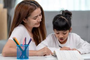 Beautiful Asian woman helping her daughter with homework at home. photo