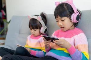 Asian siblings girl surfing net social media and playing on smartphone and digital tablet, e-learning at home photo