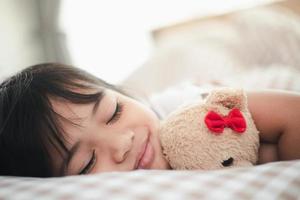 child little girl sleeps in the bed with a toy teddy bear photo