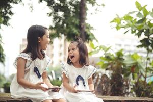 Concept kids and gadgets. Two little girls siblings sisters look at the phone and smile. They hold a smartphone watch videos, learn, play games, speak online. Internet for children. Parental control photo