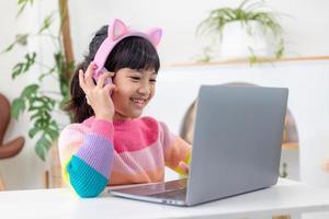 Smiling little Asian girl have a video call distant class with teacher using laptop, social distance during quarantine isolation during the Coronavirus photo