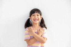 Close up of cute happy small girl isolated on white background hold hands at heart chest feel grateful, smiling little child with eyes closed pray thanking god high powers, faith concept photo
