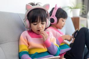 Asian siblings girl surfing net social media and playing on smartphone and digital tablet, e-learning at home photo